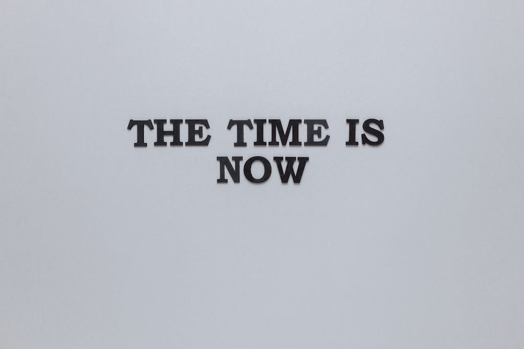 Minimalist poster with the motivational quote 'The Time is Now' on a gray background.
